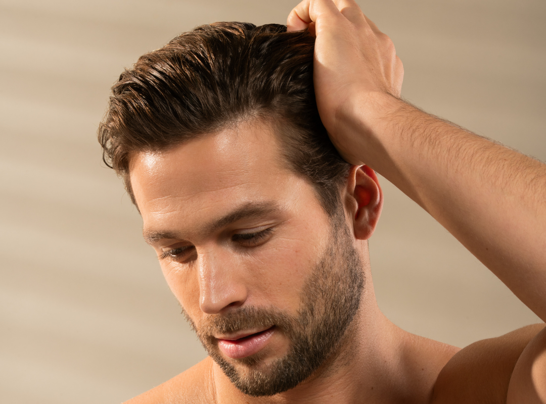 Man adjusting his hair against a neutral background