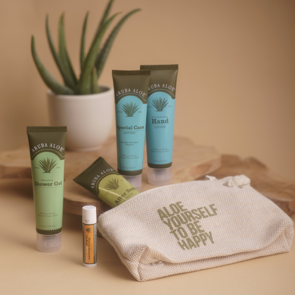 A collection of travel-sized skincare products including shower gel, lotion, sunscreen, and lip balm, displayed alongside a cotton bag with the text 'Aloe yourself to be happy'.