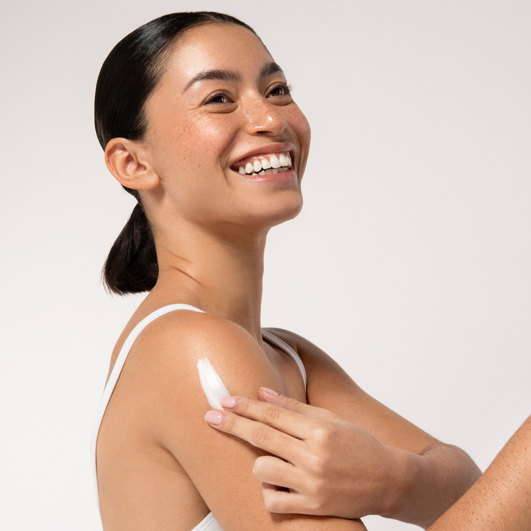 Aruba Aloe Woman applying cream on her shoulder against a plain background