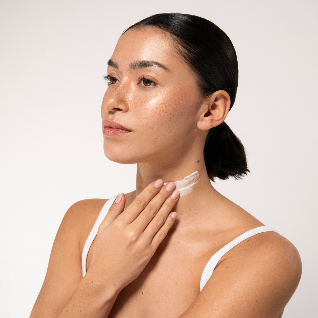 Aruba Aloe Woman applying a skincare product to her neck against a white background